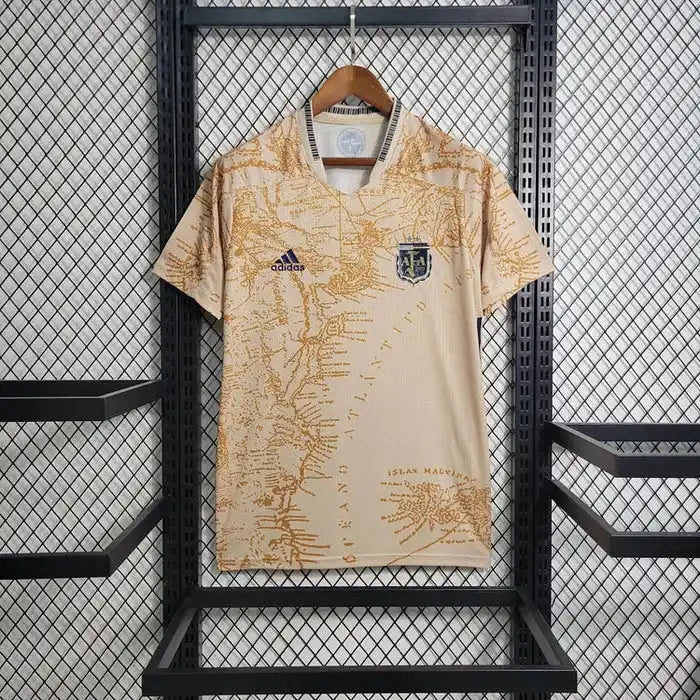 Un maillot de football beige à manches courtes avec un motif de carte marron et un écusson de l'équipe sur la poitrine gauche.